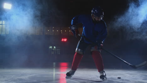 Professional-hockey-player-with-a-stick-and-a-puck-moves-on-Luda-in-skates-and-helmet-on-a-dark-background-and-smoke.-Dribbling-with-the-puck-of-a-young-man-on-the-ice-arena